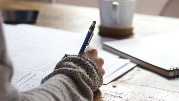 A close up shot of a hand writing notes at a table.